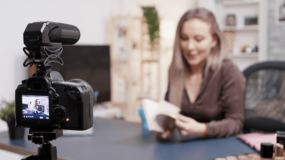 Vlogger making a book review in fron of the camera in her creative studio