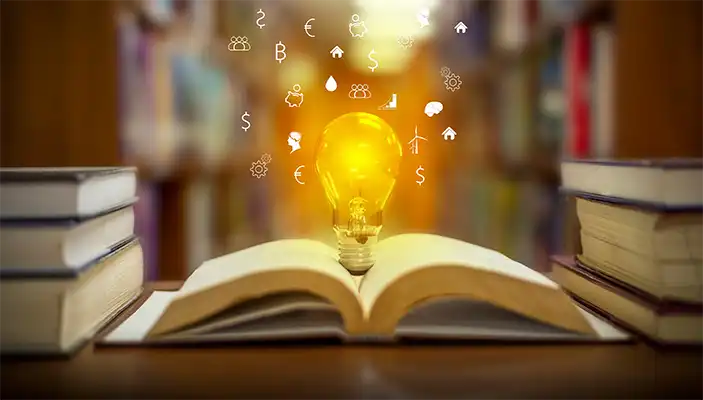 a book resting on a table with a light bulb popping out. the light is surrounded by mini white drawings of a piggy bank, money sign and gears