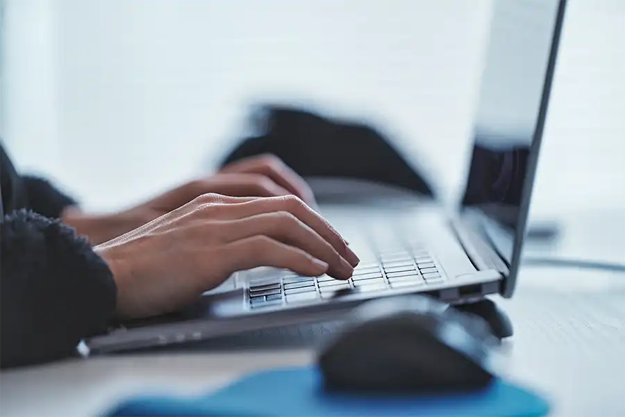 close up image of hand typing on a dark gray laptop. The image has a cool undertone.
