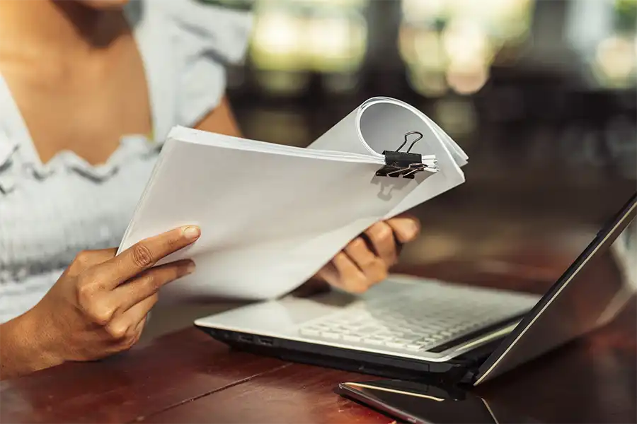 Beta reader looking over a manuscript at a wooden table with a laptop opened in front of them.