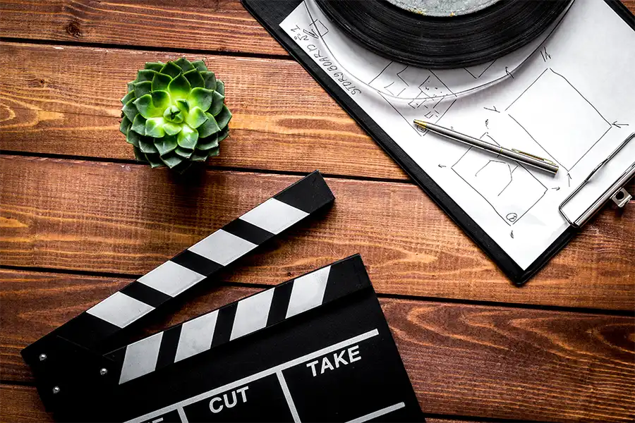a top angle image of a clapperboard, succulent and storyboard resting on a dark wooden table.