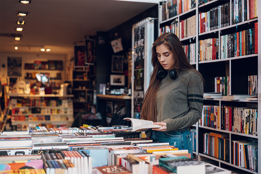 A young woman with long brown hair standing in front of a book shelf inside of a library.