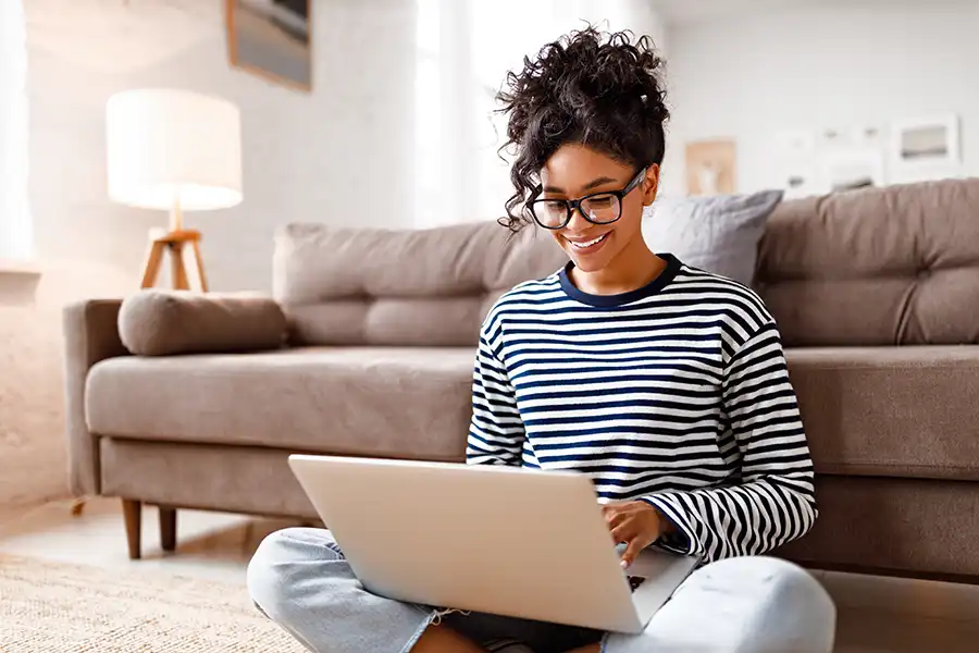 Young author sitting on the floor in front of her couch, typing on her laptop.