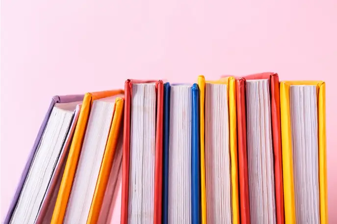 row of colorful books against a pink backdrop