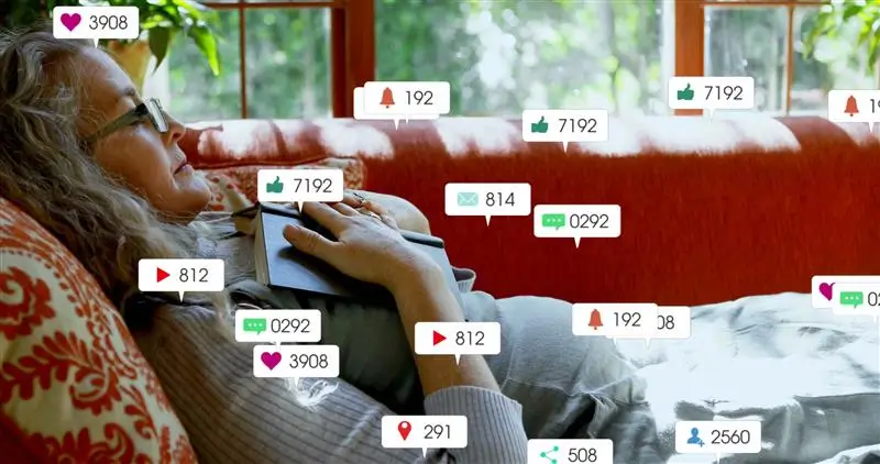 woman wearing glasses and a blazer doing research on a laptop in front of a wall of books on shelves