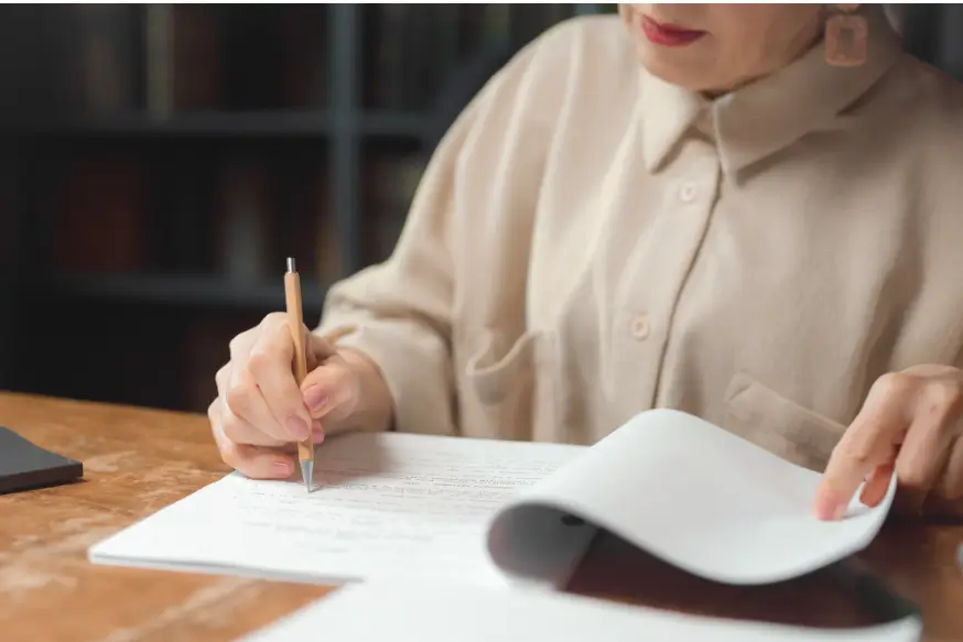 An author reviewing proof pages at a desk with a pen and manuscript, representing the author feedback stage of book production